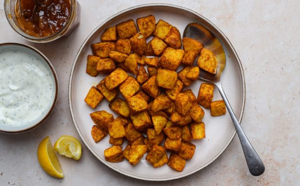 Bowl of Bombay potatoes with raita and mango chutney on the side.