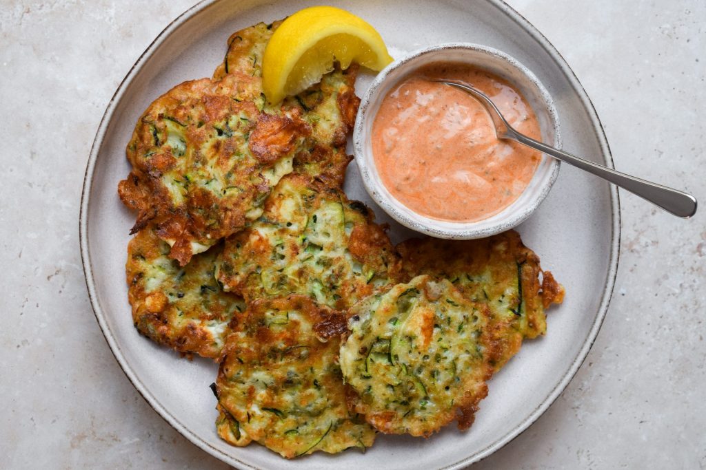 Stone plate of courgette fritters with a bowl of yogurt dip.