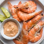 Plate of prawns with a pot of thai red curry mayonnaise and lime wedges.