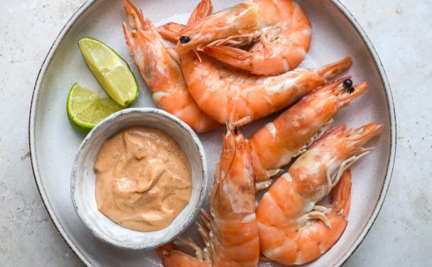 Plate of prawns with a pot of thai red curry mayonnaise and lime wedges.