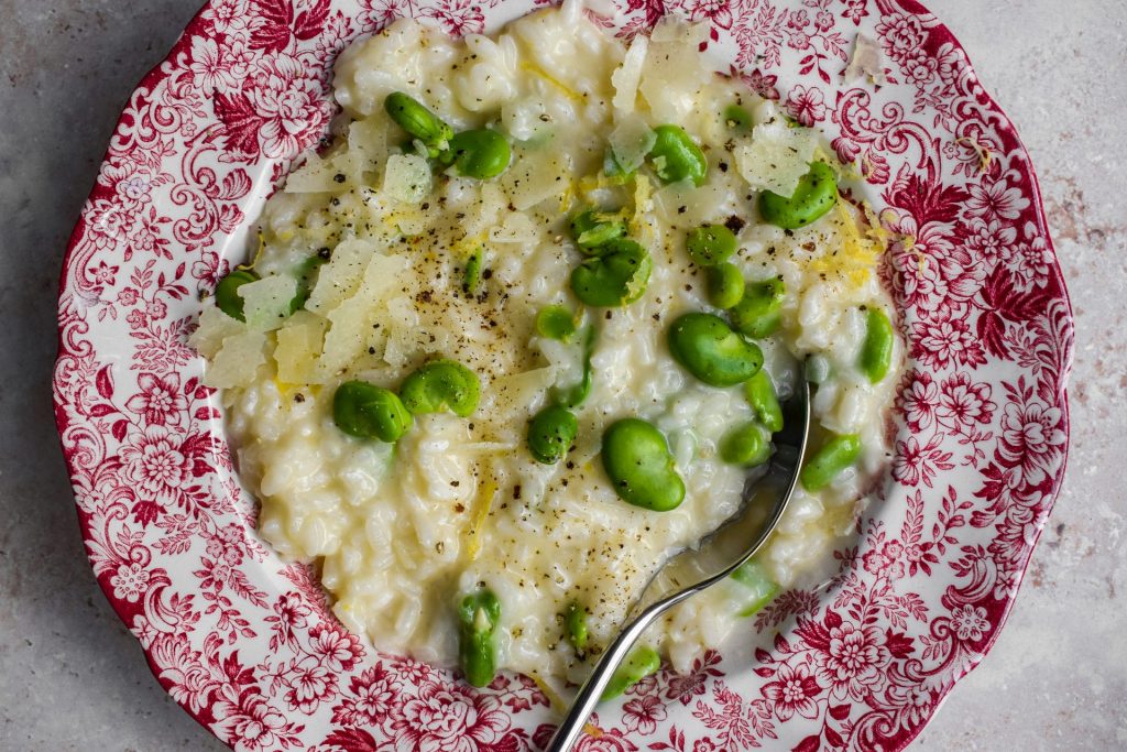 Red and white bowl of broad bean and pecorino risotto. 