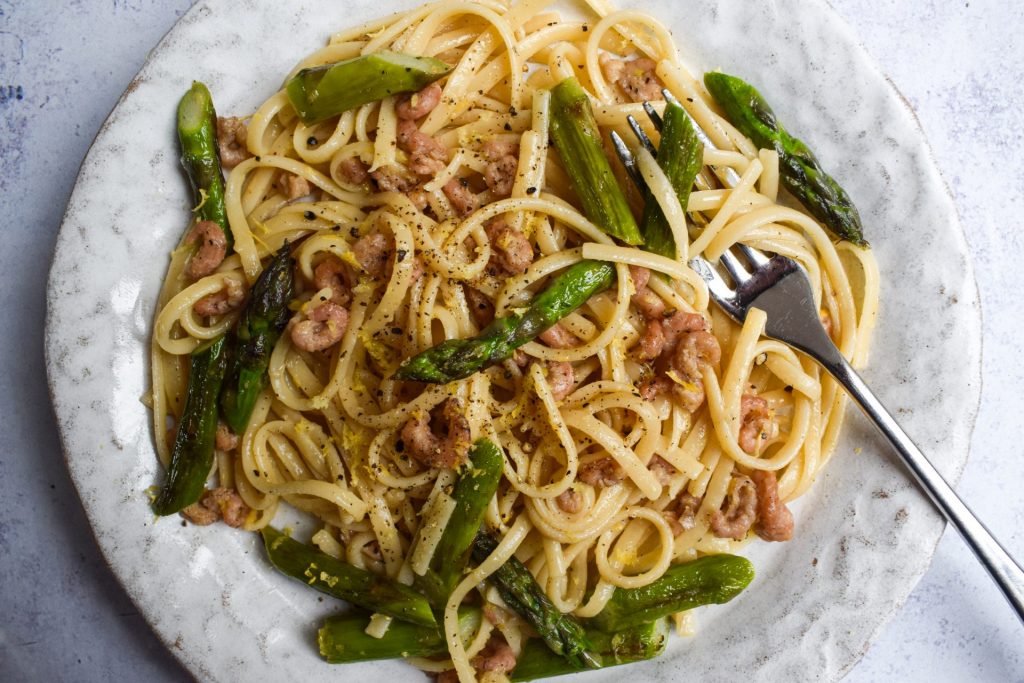 Close up of brown shrimp and asparagus pasta on a white plate.