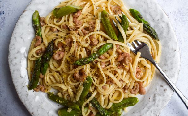 Close up of brown shrimp and asparagus pasta on a white plate.