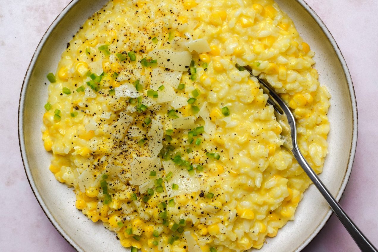 Bowl of corn risotto topped with cheese and chopped green chilli.